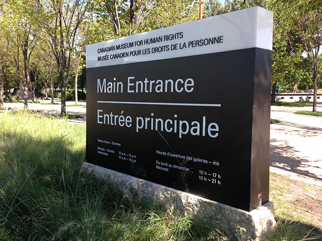 Black and white sign saying Main entrance along with information about the Museum opening hours